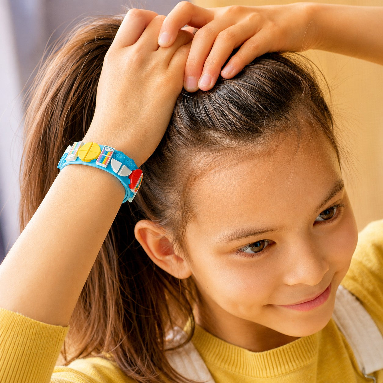 Child wearing LEGO DOTS Rainbow Bracelet while styling hair, close-up view
